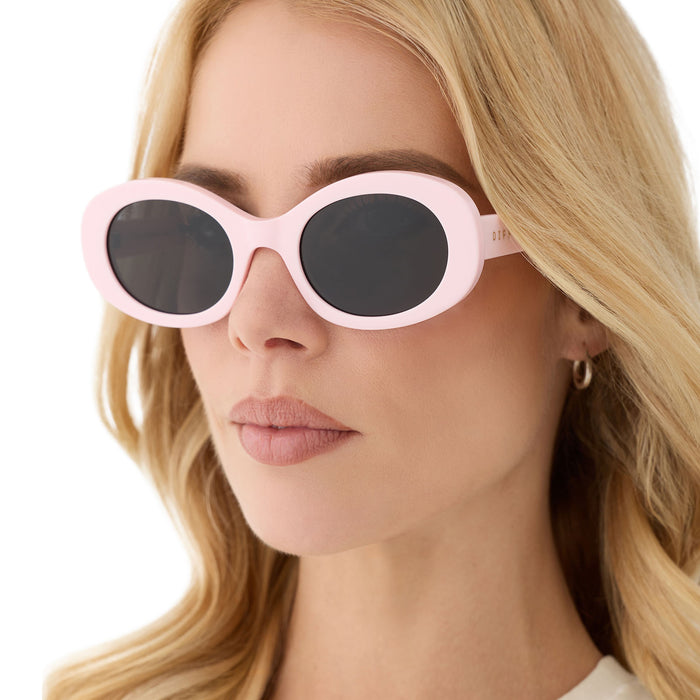 on model - female wearing diff eyewear featuring the lainey oval sunglasses with a powder pink frame and grey polarized lenses angled view