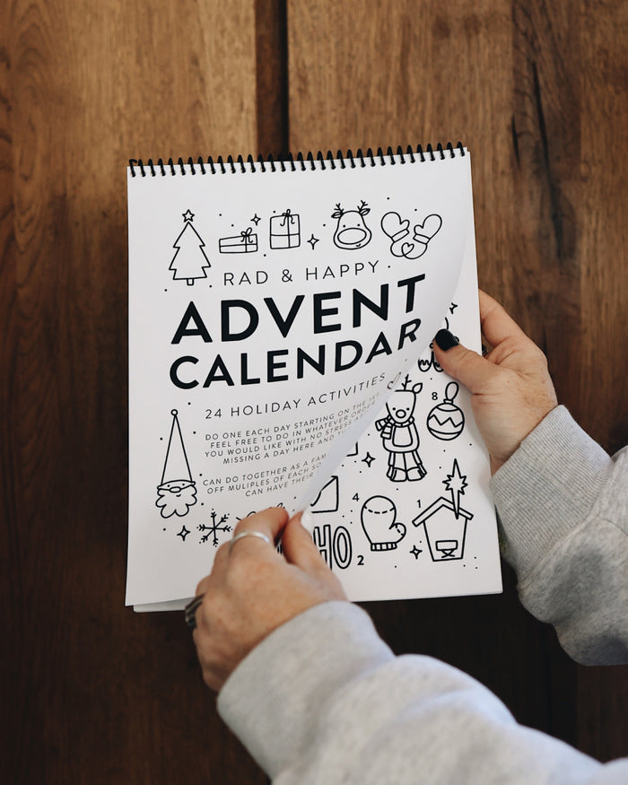 Person holding a spiral-bound Advent calendar with black and white illustrations on a wooden surface