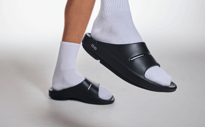 Women's OOahh Slide Sandal - Black close up of shoe on model lifting foot up in studio | lifestyle