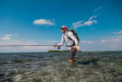 An angler fly fishing in clear knee high water with a bright blue sky.