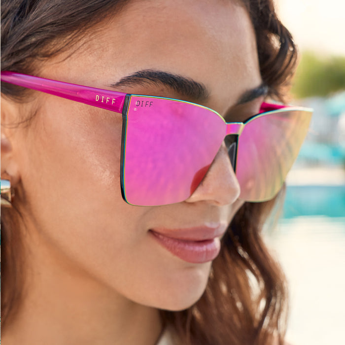 lifestyle - female at the beach wearing diff eyewear featuring the goldie cat eye sunglasses with a bright tulip frame and pink rush mirror lenses angled view
