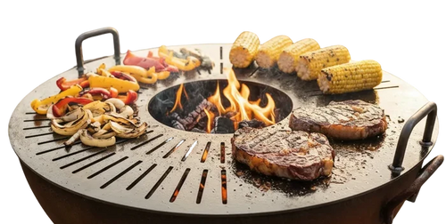 A round outdoor fire pit grill with handles sits on a gravel patio, cooking two steaks, corn on the cob, and sliced peppers and mushrooms over an open flame. Two patio chairs and stacked firewood are visible in the background of this backyard scene.