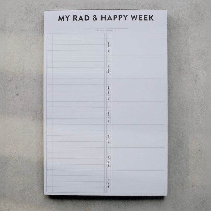 Weekly planner pad titled 'My Rad & Happy Week' on a gray surface