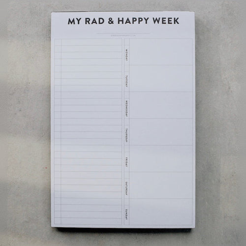 Weekly planner pad titled 'My Rad & Happy Week' on a gray surface