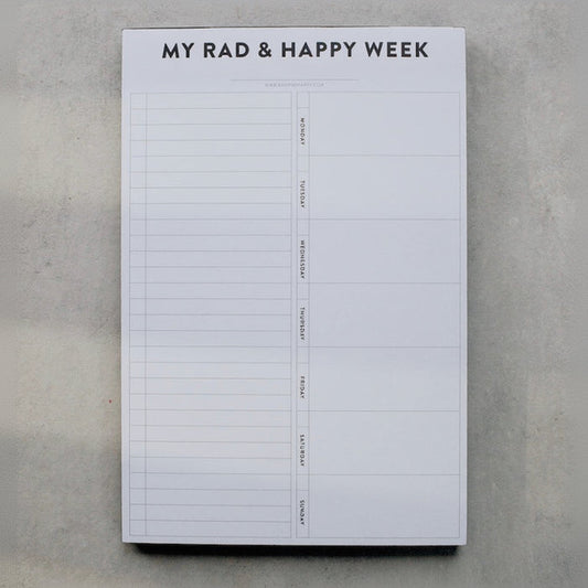 Weekly planner pad titled 'My Rad & Happy Week' on a gray surface