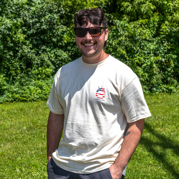 Man wearing sunglasses and a t-shirt with Cortland Line logo, standing in a grassy area with trees in the background.