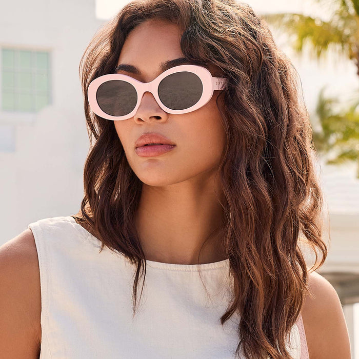 lifestyle - female at beach resort wearing wearing diff eyewear lainey oval sunglasses with a powder pink frame and grey polarized lenses front view