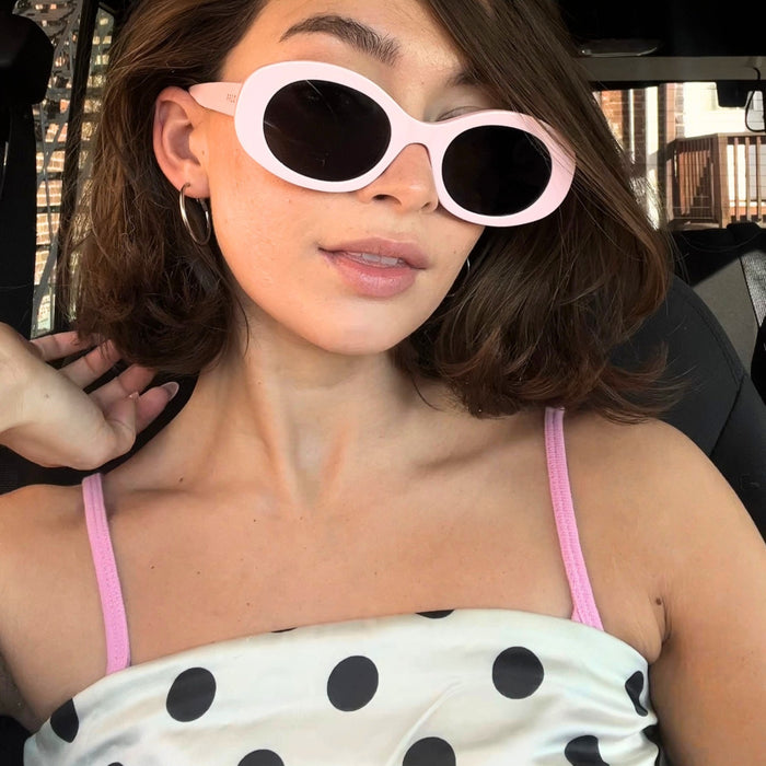 brunette with chic bob hair cut wearing white and black polka dot top with pastel light pink oval shaped sunglasses