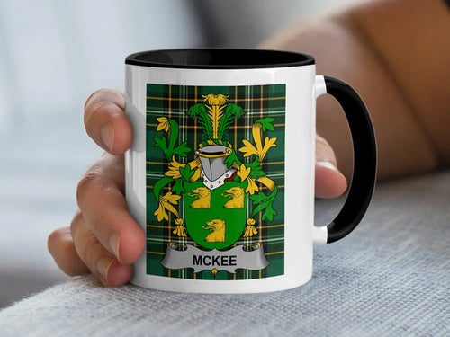 White mug with black rim featuring the McKee family crest on a tartan background.