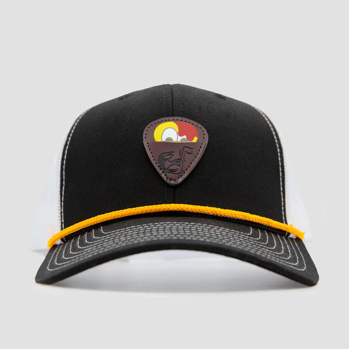 A black and white trucker hat with a yellow rope across the brim and a brown patch featuring a stylized cartoon bird on the front.