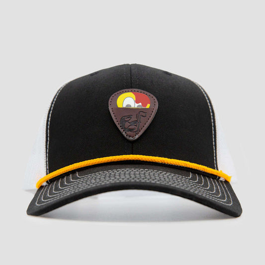 A black and white trucker hat with a yellow rope across the brim and a brown patch featuring a stylized cartoon bird on the front.
