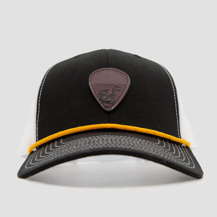 A black and white trucker cap with a brown leather patch featuring an emblem on the front and a yellow cord running across the base of the front panel.