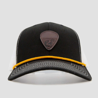 A black and white trucker cap with a brown leather patch featuring an emblem on the front and a yellow cord running across the base of the front panel.