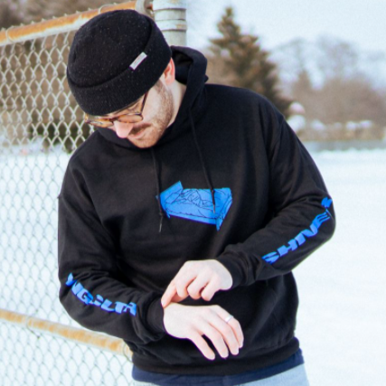Black pullover hoodie with artwork of a blue bed on the chest. Along the left sleeve, "YNG CLTR" is written in blue. On the right sleeve, "SHIVER" is written in blue. An individual is wearing the hoodie in front of a fence, with snow on the ground.