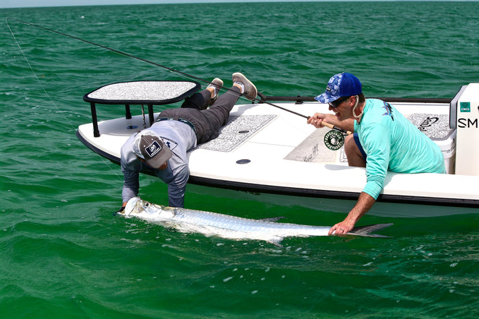 Two individuals are leaning over a boat and holding onto a tarpon.