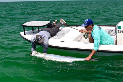 Two individuals are leaning over a boat and holding onto a tarpon.