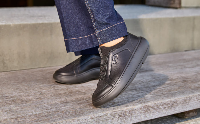 Person wearing black slip-on shoes and blue jeans sitting on a wooden bench | lifestyle