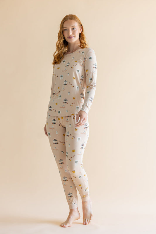 A woman modeling a two-piece long-sleeve pajama set with an all-over Gilmore Girls inspired print on a warm cream background, set against a solid light beige studio backdrop.