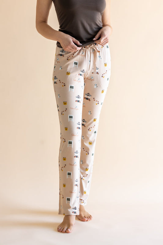 A person wearing cream-colored lounge pants with a Gilmore Girls inspired pattern, paired with a dark gray top, standing against a solid beige background.