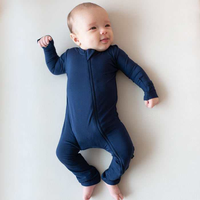 Infant laying on an Oat surface while wearing a  Zippered Romper in Navy